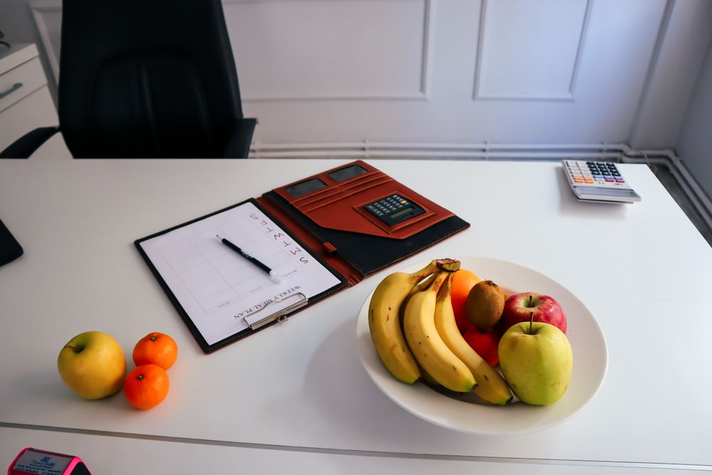 Büroschreibtisch mit einer Schale voller Bananen, Äpfel und Mandarinen